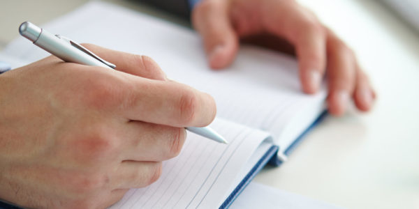 Businessman hand with pen over open notebook making report